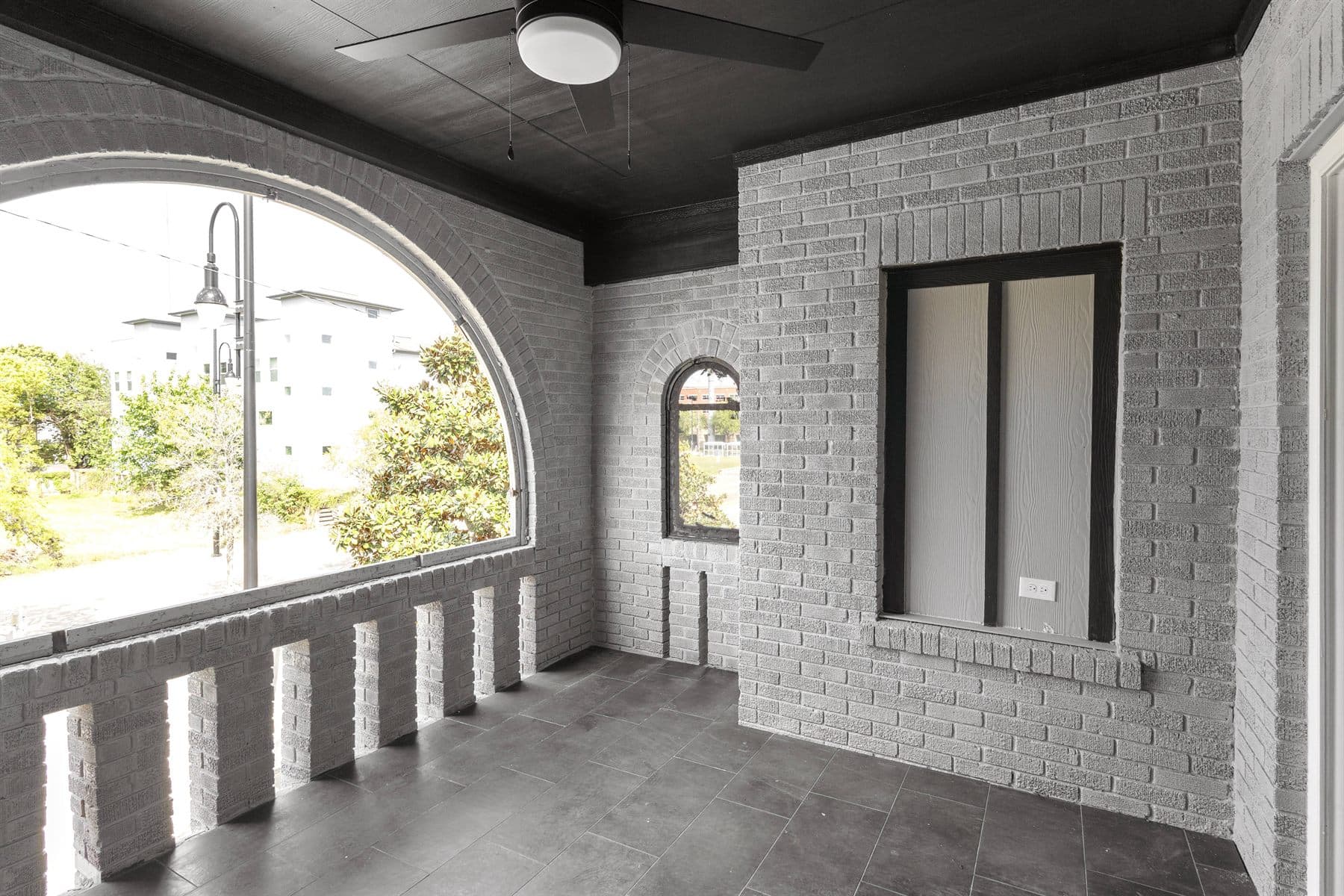 White brick arched porch nook with round-top windows over a tree-lined street, finished by the Reborn group