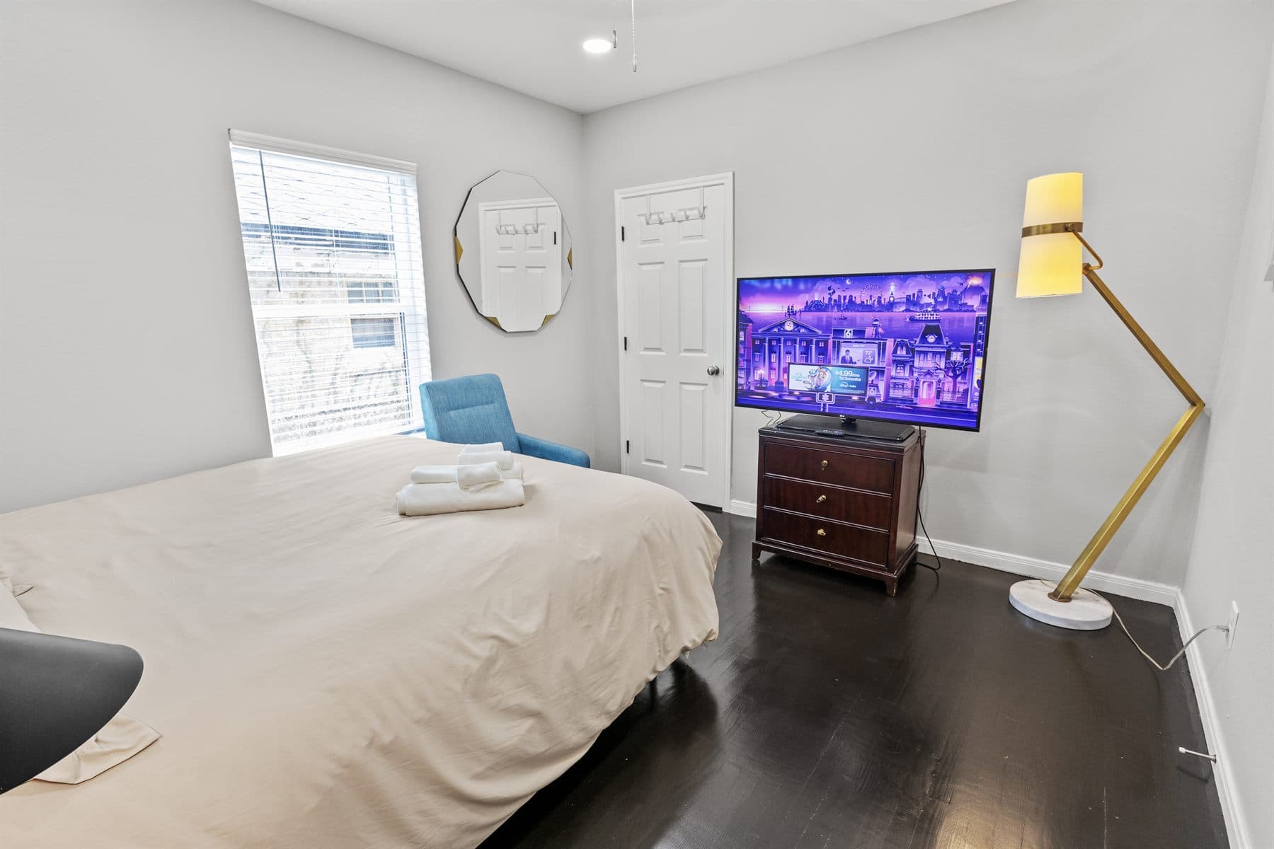 Bedroom with white bedding, mounted TV and gold floor lamp, finished by the Reborn group