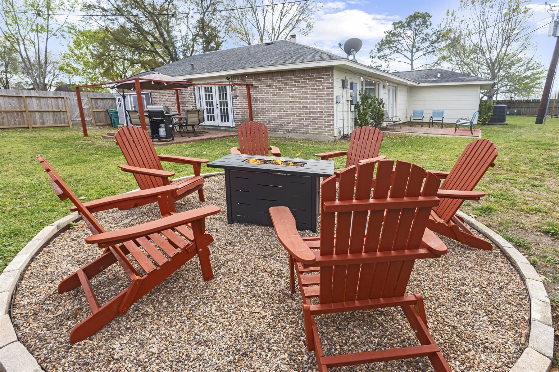 Stone fire pit circle with red Adirondack chairs, flames lit, finished by the Reborn group