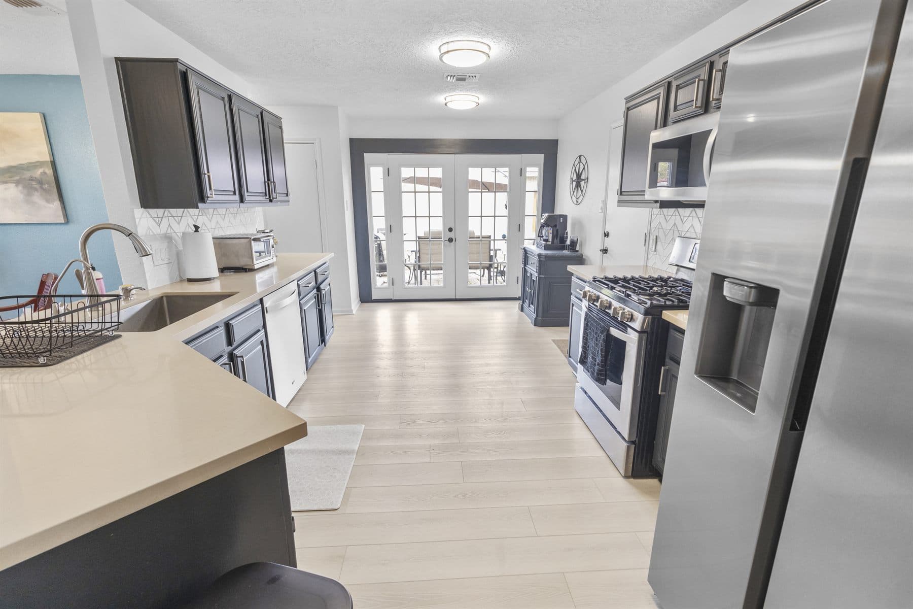 Long kitchen with dark cabinets, stainless fridge and French doors, finished by the Reborn group