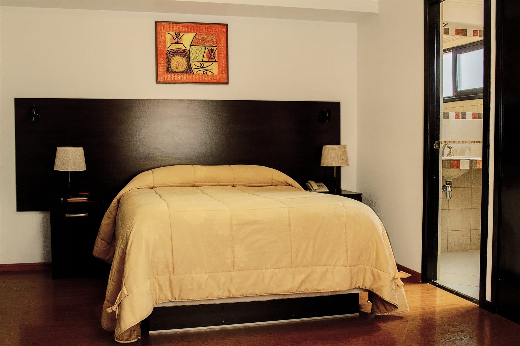 Bright bedroom with gold bedding and dark wood headboard, finished by the Reborn group