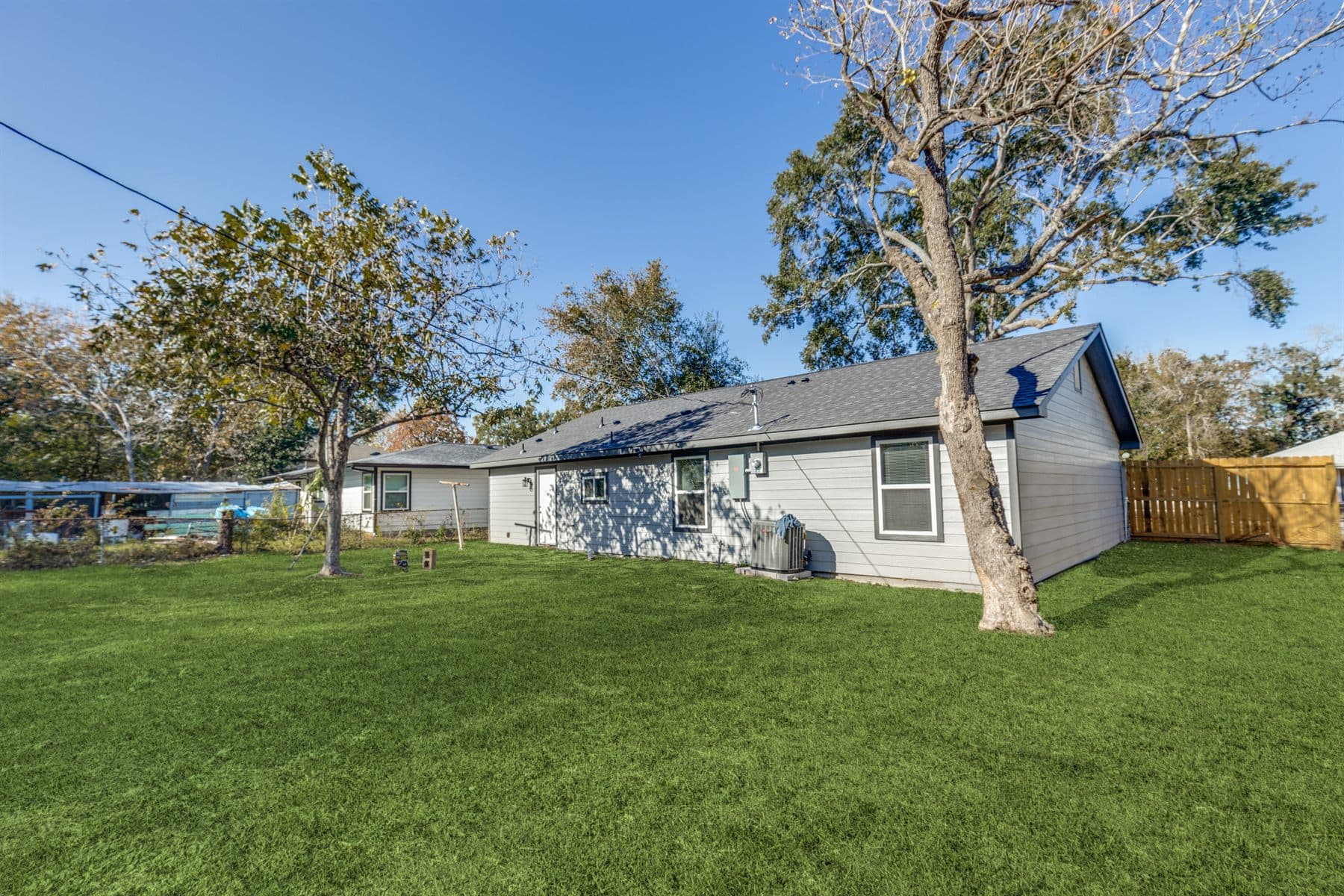 Wide manicured lawn under mature oak trees with wood privacy fence, finished by the Reborn group