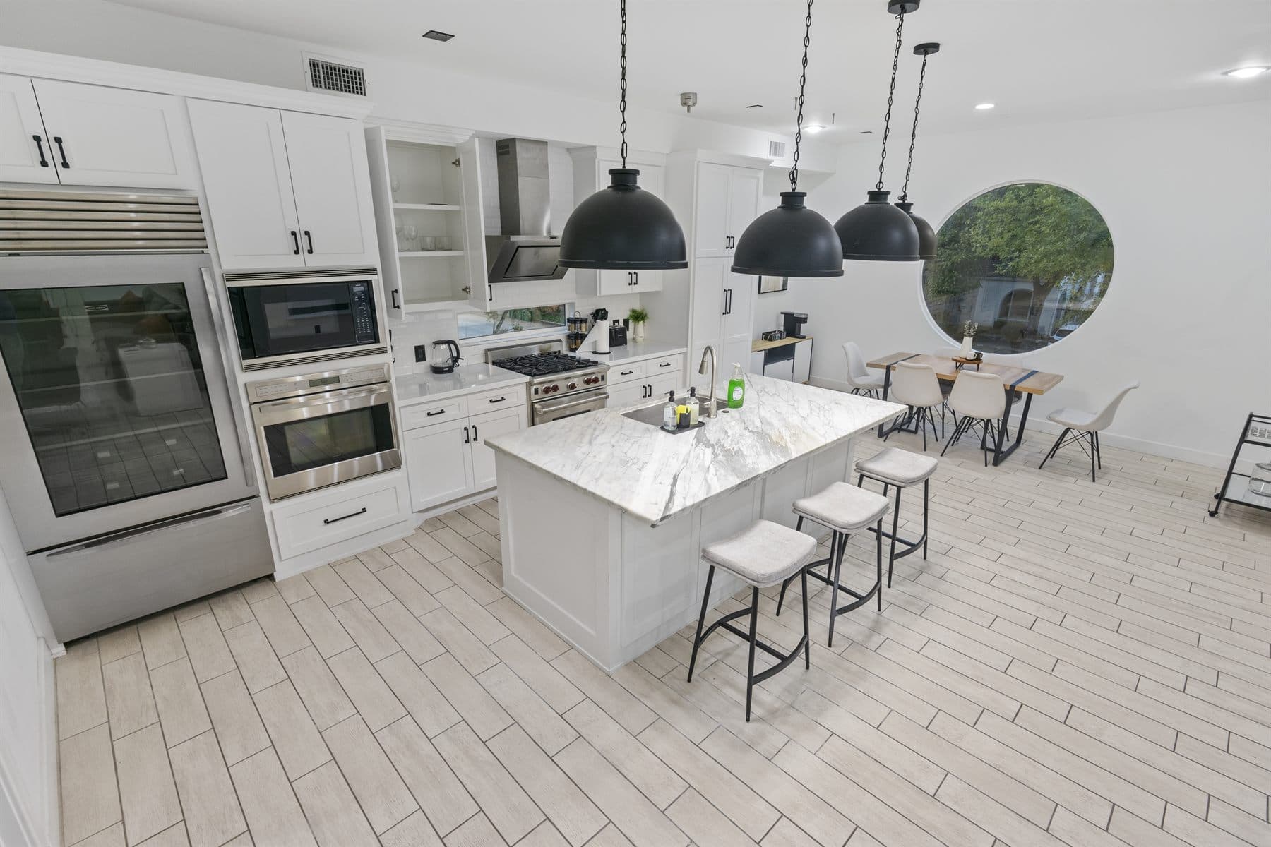 White kitchen with marble island, black pendant lights and stainless range, finished by the Reborn group