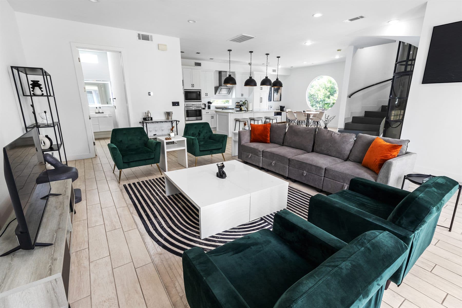 Open living area with green velvet chairs and a round picture window, finished by the Reborn group