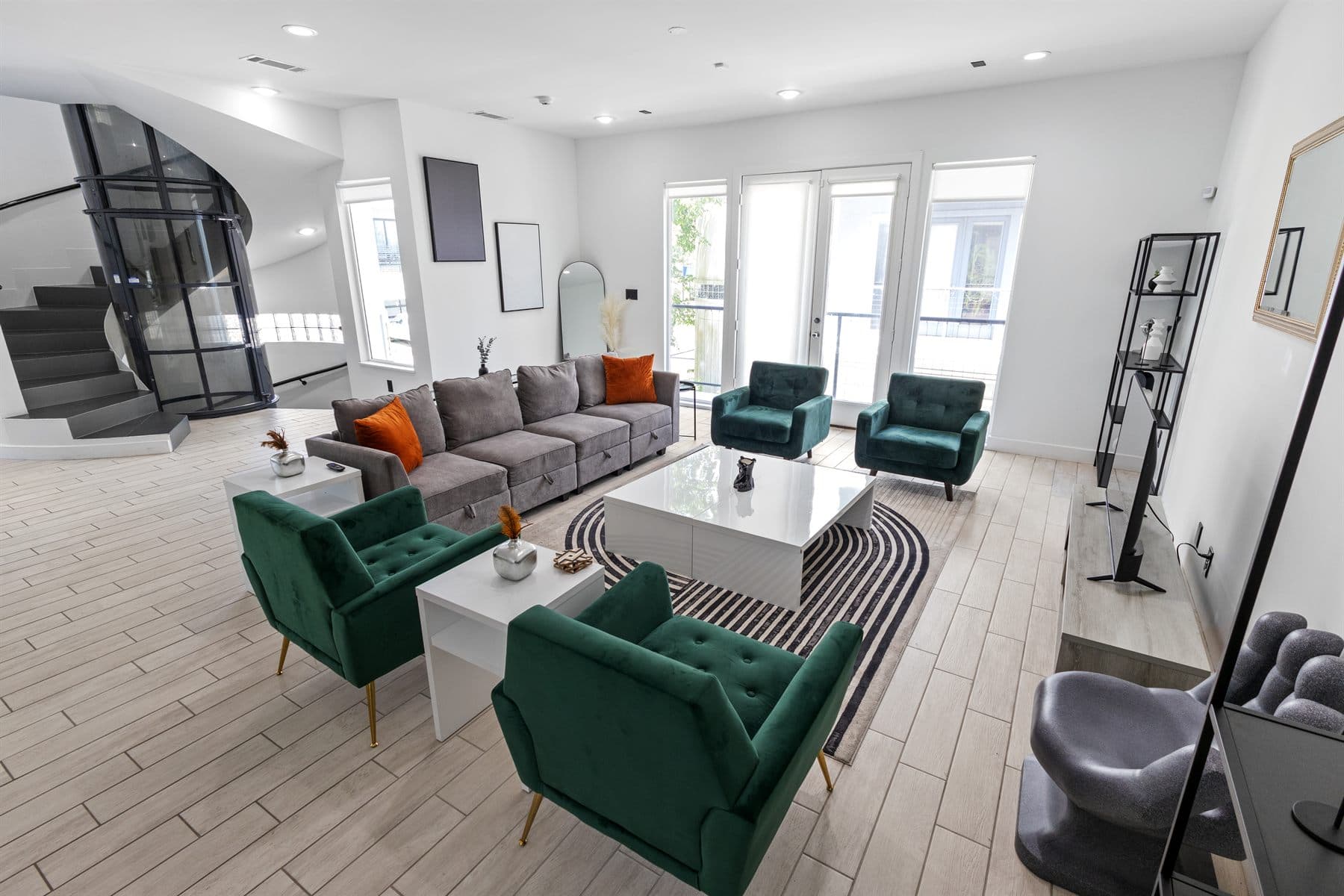 Great room with sectional, emerald armchairs and spiral staircase beyond, finished by the Reborn group