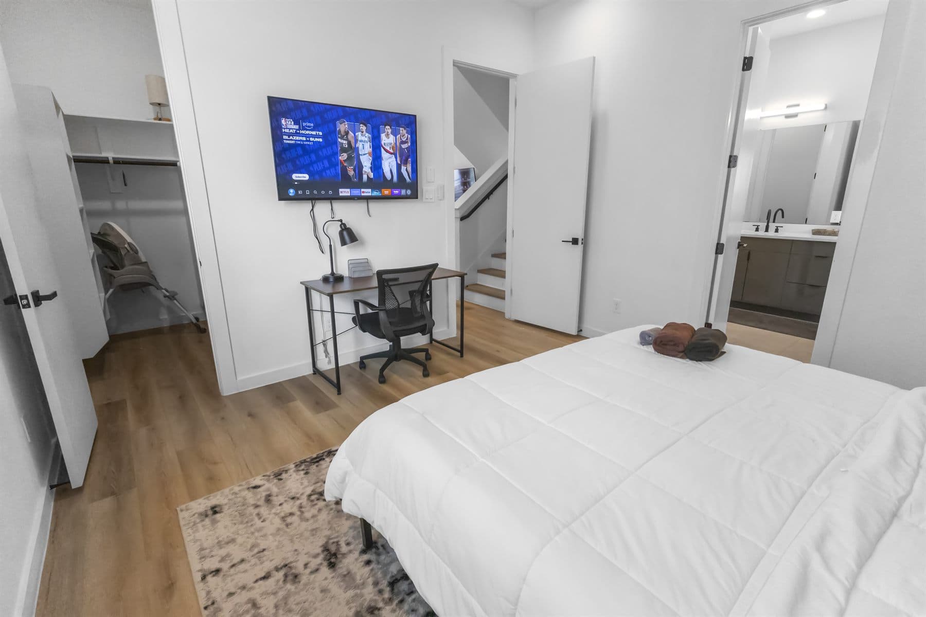 Bedroom with desk nook, wood accent wall and white bedding, finished by the Reborn group