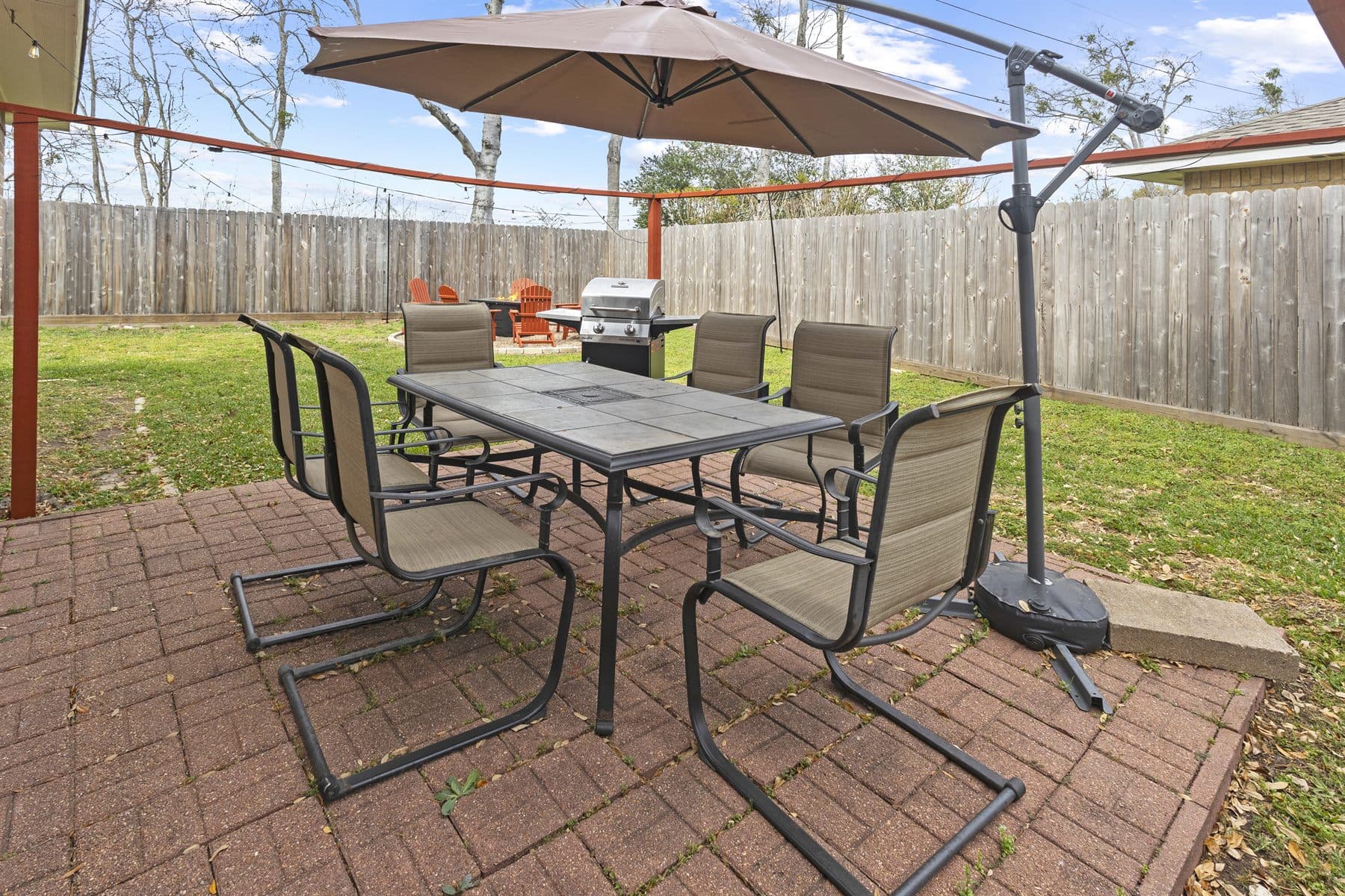 Brick paver dining patio with umbrella table beside a wood privacy fence, finished by the Reborn group