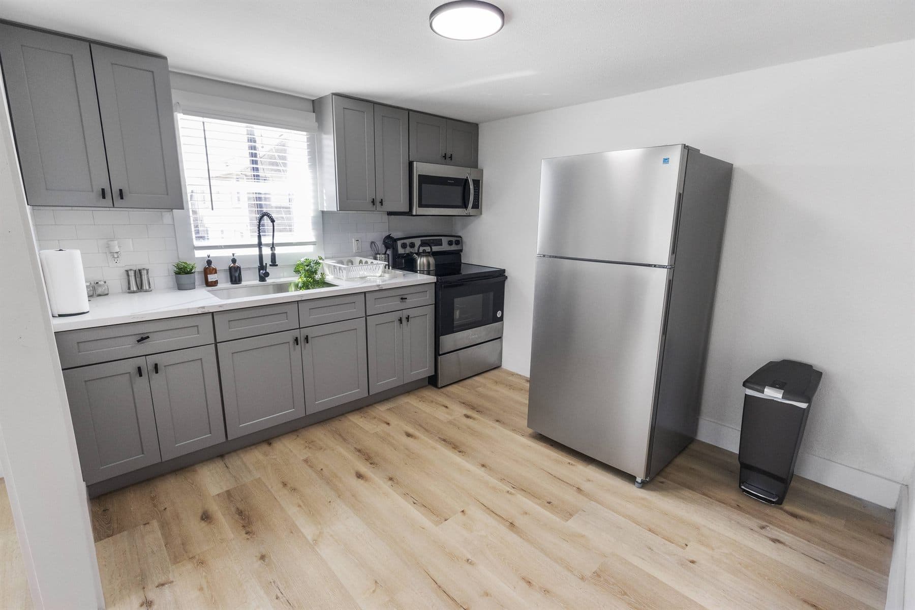 Gray shaker kitchen with white quartz counter and stainless fridge, finished by the Reborn group