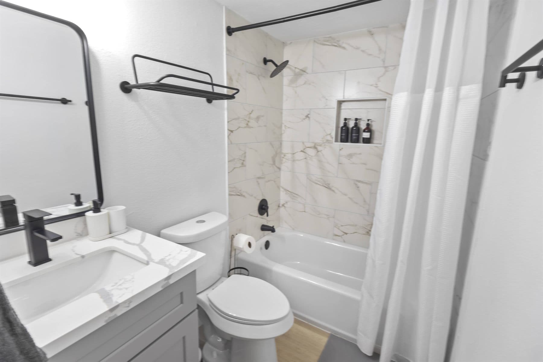 Tub and shower with marble-look tile and matte black fixtures, finished by the Reborn group