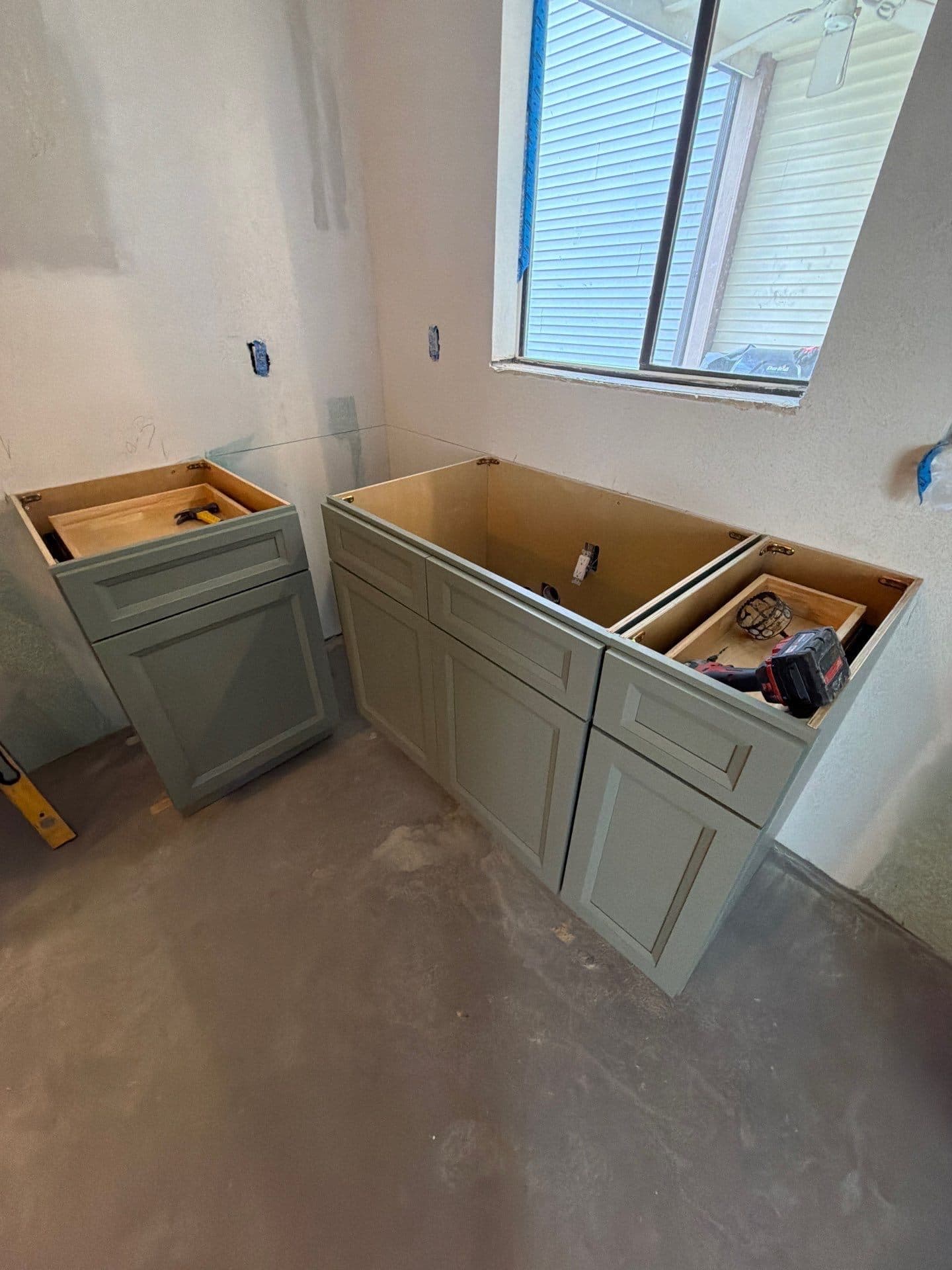Pair of sage-green vanities being set beneath the bathroom window