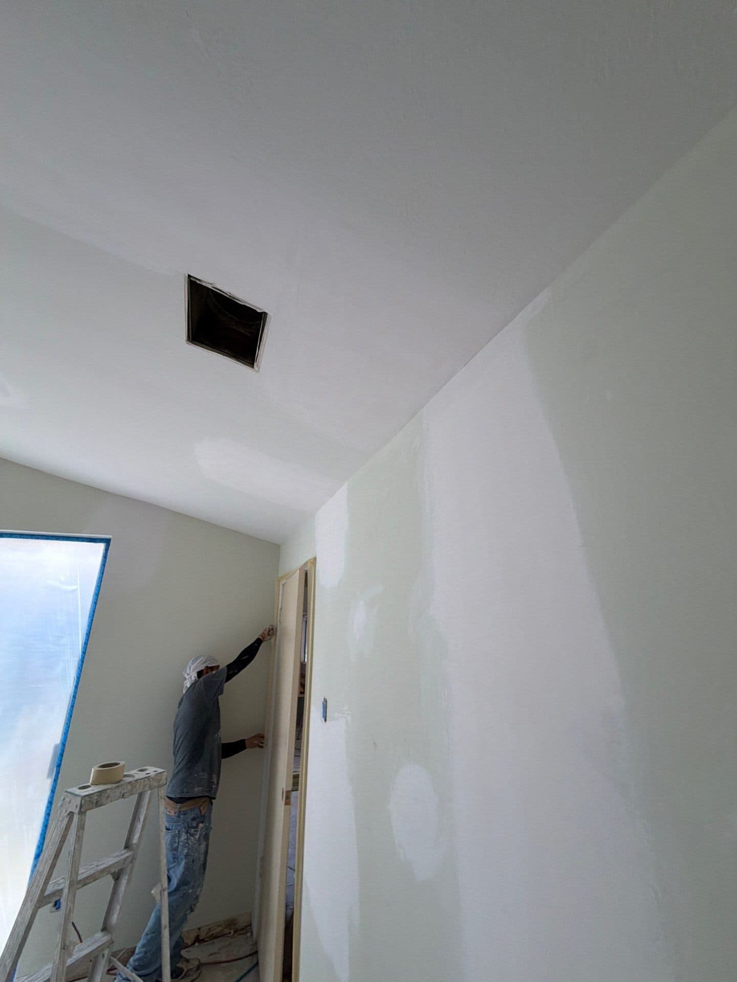 Finisher on a ladder detailing fresh skim coat under the vaulted ceiling