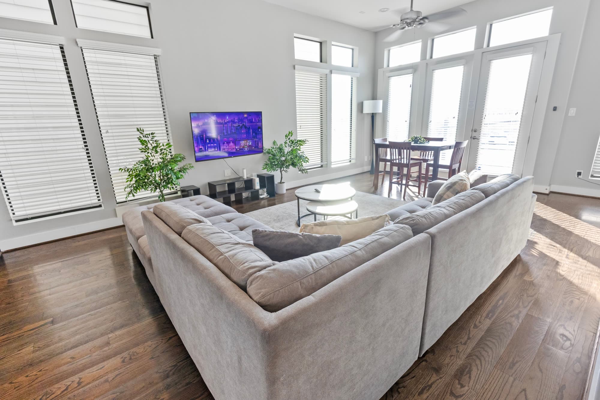 Living room with gray sectional and a sunlit dining nook, furnished by the Reborn group