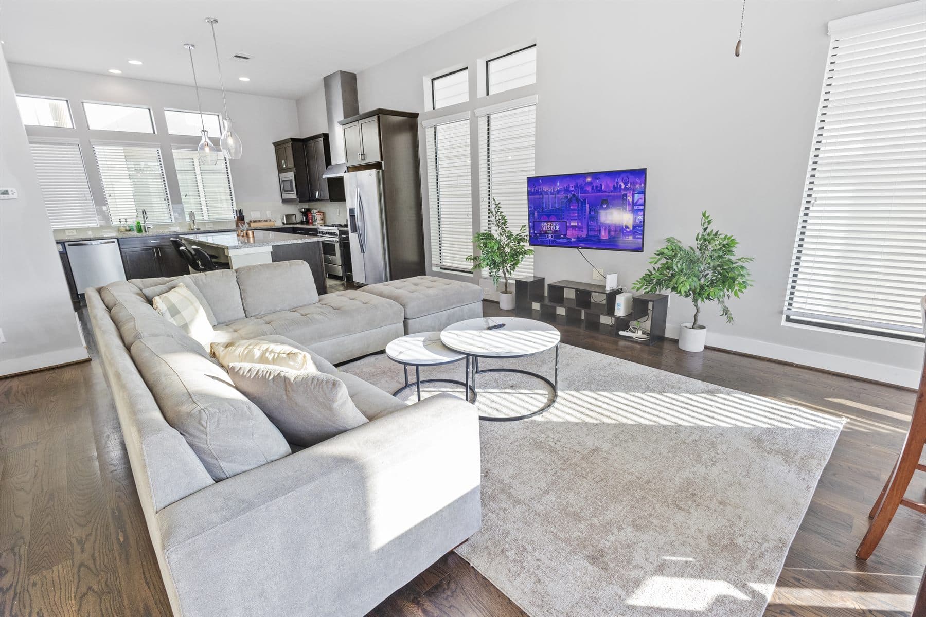 Open living room with gray sectional and dark kitchen beyond tall windows, finished by the Reborn group