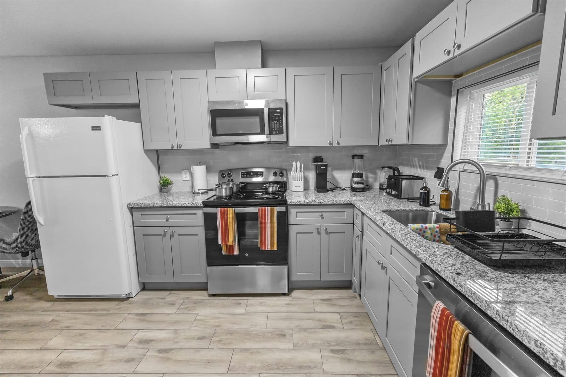 Gray shaker kitchen with stainless appliances and window over sink, finished by the Reborn group