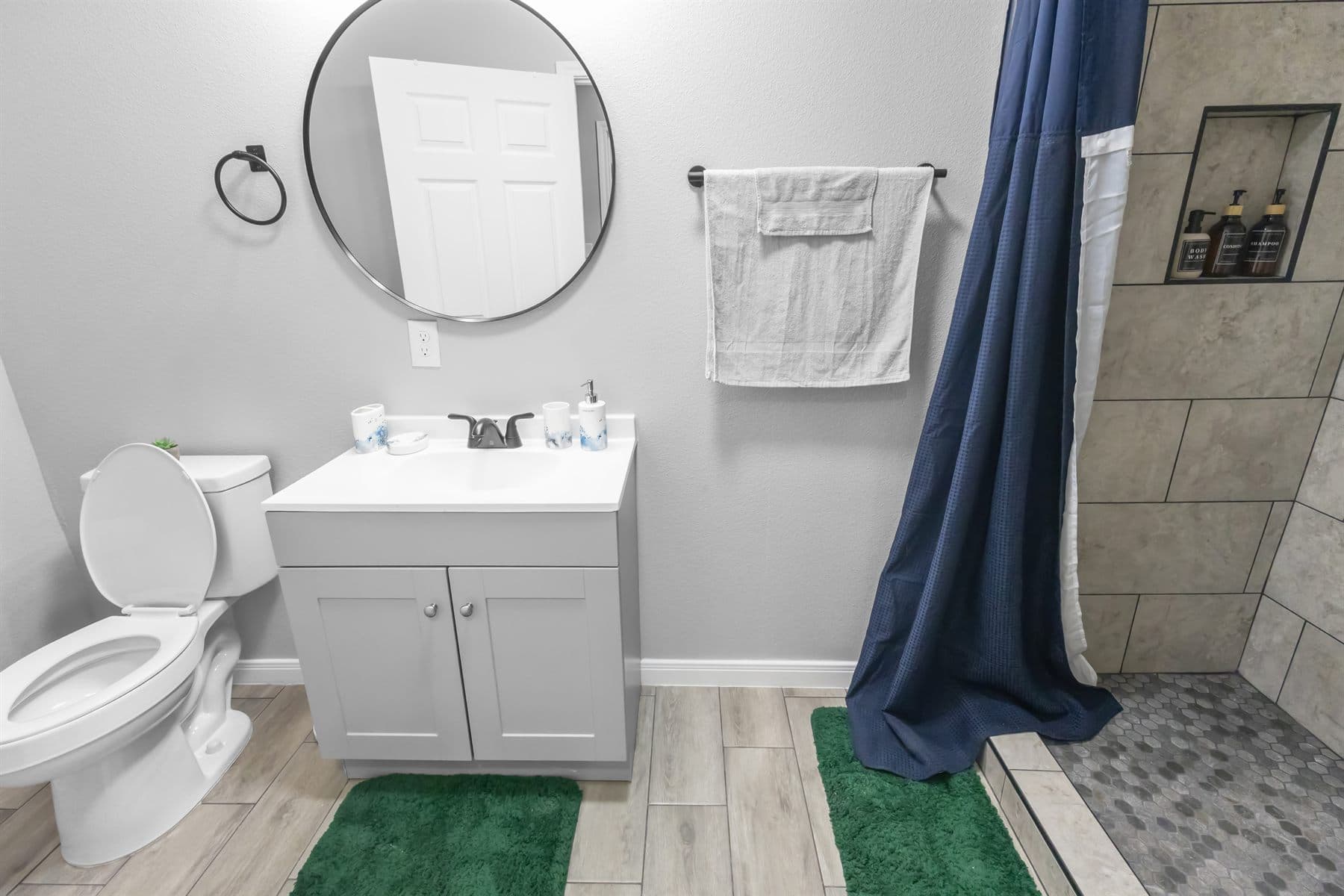 Tile shower with matte black fixtures and round mirror, finished by the Reborn group