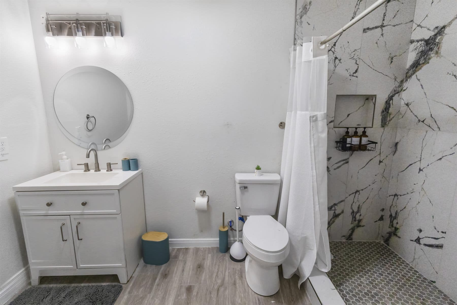 Bath with marble-look shower surround and round mirror, finished by the Reborn group